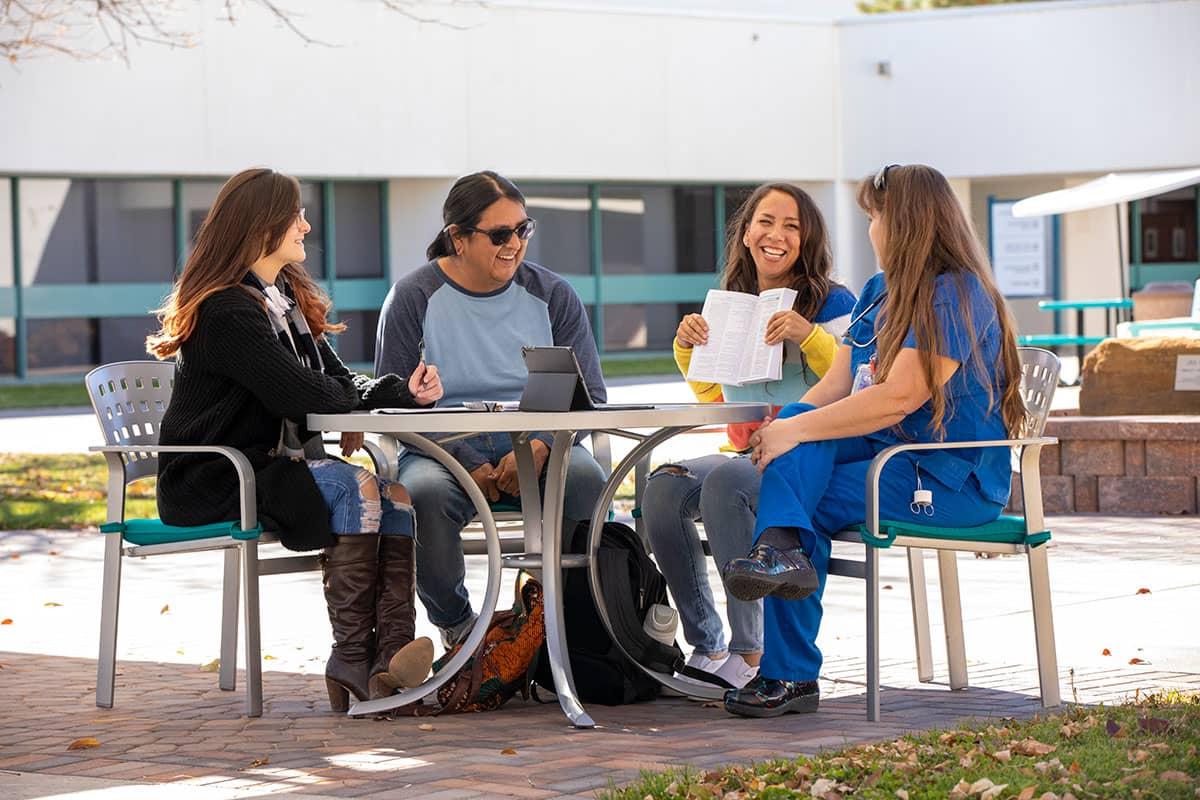 四个火博体育的学生坐在外面的一张桌子旁交谈和微笑.